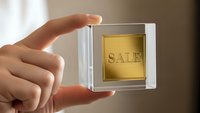 Hand holding transparent glass cube with golden sale label inside, promotional marketing concept for retail business advertising campaigns.