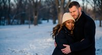 Loving interracial couple embracing in snowy winter park during golden hour sunset. Romantic outdoor portrait for engagement and relationship content.