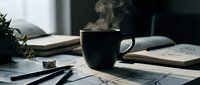 Steaming black coffee mug on a desk surrounded by open notebooks, pencils, and sketches in a moody, creative workspace atmosphere.