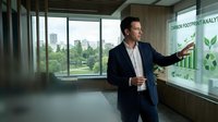Caucasian male business executive presenting carbon footprint analytics on interactive screen in modern eco-friendly office with city park view.
