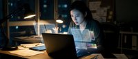 Young Asian businesswoman working late at night in modern office using laptop computer for overtime project deadline with focused concentration.