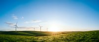 Wind turbines generating clean renewable energy on rolling green hills at golden hour sunset with clear blue sky for sustainable power concepts.