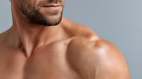 Close-up of muscular Caucasian man's shoulder and neck with stubble beard against gray background, showcasing defined physique for fitness and wellness content.