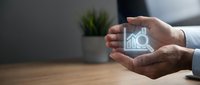 Hand holding transparent glass cube with house and magnifying glass icon for property search and real estate investment concept.