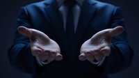 Businessman in dark blue suit extending open hands forward against black background, offering help or opportunity in corporate setting.