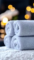 Soft white spa towels stacked with warm bokeh lights in background creating relaxing atmosphere for wellness, massage, and hotel amenities promotion.