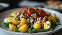 Fresh tuna salad with boiled potatoes, green beans, cherry tomatoes, and hard-boiled eggs on white plate, perfect for healthy lunch or dinner.