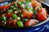 Fresh cherry tomatoes glazed with Asian sauce, garnished with chopped green onions and sesame seeds in blue ceramic bowl, close up view of appetizing side dish.