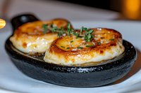 Seared sea scallops with caramelized golden crust garnished with fresh herbs served in black cast iron pan, close up view showing texture and juicy interior.