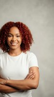 Confident young African American woman with curly red hair smiling with arms crossed wearing white t-shirt against neutral background for business portrait.