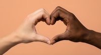 Two diverse hands forming heart shape symbol representing unity love and togetherness against warm peach background for social campaigns.