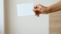 Hand holding blank white card or paper against neutral background for messaging, advertising, or promotional content display.