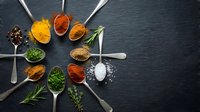 Colorful spices and herbs arranged in metal spoons on dark slate background. Culinary ingredients for cooking and seasoning food preparation.