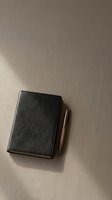 Closed black leather notebook with metal pen on neutral beige textured surface, overhead view for business, planning, and office design projects.