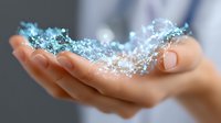 Gentle female hands holding glowing blue magical sparkles and light particles floating in air against dark background, creating ethereal atmosphere.