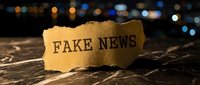 Torn paper with fake news text on wooden surface against blurred city lights background. Media misinformation and journalism concept for editorial use.