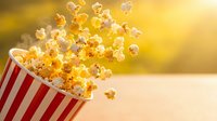 Fresh popcorn bursting from red striped container with golden sunlight background for entertainment and snack advertising concepts.