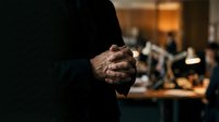 Professional businessman with clasped hands in modern office environment during evening hours with warm ambient lighting and blurred workspace background.