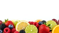 Fresh mixed fruits and berries border on white background with strawberries, blueberries, raspberries, blackberries, orange and lime slices for healthy eating.