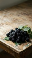 Fresh ripe blackberries with green leaves arranged on rustic wooden surface. Organic berries for culinary, food styling, and recipe content.