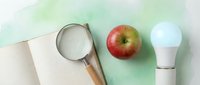 Overhead view of kitchen essentials including sieve, fresh red apple, LED bulb and notebook on green and white background for cooking and healthy lifestyle concepts.