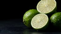 Fresh green limes whole and sliced in half showing juicy citrus flesh on dark slate background for cooking and beverage preparation.
