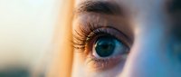Close-up of woman's blue eye with long eyelashes in warm golden light. Natural beauty and skincare concept for cosmetics and wellness advertising.