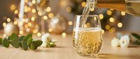Champagne pouring into glass with festive bokeh lights and holiday decorations in background, suitable for celebrations and event marketing.