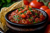 Fresh homemade salsa with diced tomatoes, cilantro and spices served in rustic clay bowl with tortilla chips and whole tomatoes for appetizer or snack.