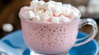 Pink hot chocolate with marshmallows in glass mug on blue saucer, cozy winter drink for cafes and seasonal marketing campaigns.