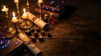 Mystical fortune telling setup with tarot cards, burning candles, ancient scrolls and magical accessories on dark wooden table for divination practices.