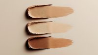 Smooth foundation or concealer smears showing different skin tone shades from light to medium on neutral beige background, makeup swatches for cosmetics industry.