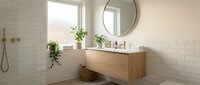 Modern bathroom with floating wooden vanity, round mirror, white subway tile walls, potted plants, and natural light from window.