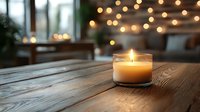 Glowing aromatic candle in glass jar on wooden table with blurred warm bokeh lights background creates cozy atmosphere for relaxation and meditation.