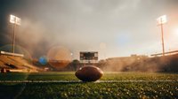 American football on grass field in stadium with bright floodlights and lens flare effects during golden hour creating dramatic sports atmosphere.