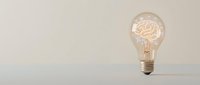 Glowing light bulb with brain filament on wooden surface against beige wall background representing creativity, innovation and bright ideas for business concepts.