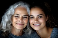 Close-up portrait of senior woman with gray hair and young Hispanic woman with curly hair smiling at camera, representing family bond and generations.