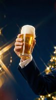 Man in formal business suit holding glass of golden beer with foam head against dark blue background with golden bokeh lights and sparkles.