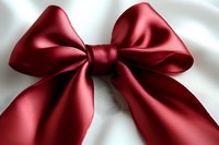 Elegant red satin bow with symmetrical loops and tails isolated on white background, featuring rich texture and subtle sheen for festive decoration and gift wrapping.