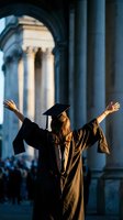 Female graduate celebrating with raised arms in cap and gown at university campus with classical columns during golden hour sunset lighting.