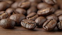 Freshly roasted coffee beans scattered on wooden surface with selective focus showing rich brown color and natural texture for cafe and coffee shop marketing.