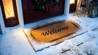 Welcome doormat at snowy front door decorated with Christmas wreath, warm holiday entrance scene perfect for winter and seasonal home decor concepts.
