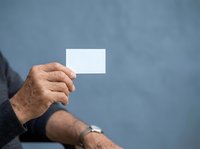 Senior male hand holding blank white business card against blue background, suitable for corporate branding and professional mockup designs.