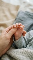 Tender moment of parent holding newborn baby feet in cozy knitted clothing on soft blanket showcasing precious bond between mother and infant child.