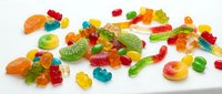 Colorful assorted gummy candies and jelly sweets scattered on white background. Variety of fruity gummy bears, worms and shapes for confectionery designs.