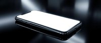 Modern black smartphone with blank white screen lying on reflective surface with dramatic lighting and bokeh background for technology mockups.