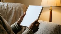 Woman in cozy sweater holding blank white tablet while relaxing on bed with warm lamp lighting, suitable for technology, lifestyle, and home comfort concepts.