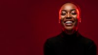 Happy young African American woman laughing with joy against red background wearing black turtleneck sweater for lifestyle and wellness content.