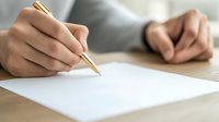 Young Asian woman's hands holding gold pen over blank white paper on wooden desk, ready for writing letter, note or signing document in bright daylight.