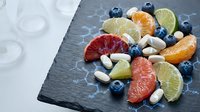 Fresh citrus fruit slices with blueberries and white beans arranged on dark slate board for healthy eating and nutrition concepts.